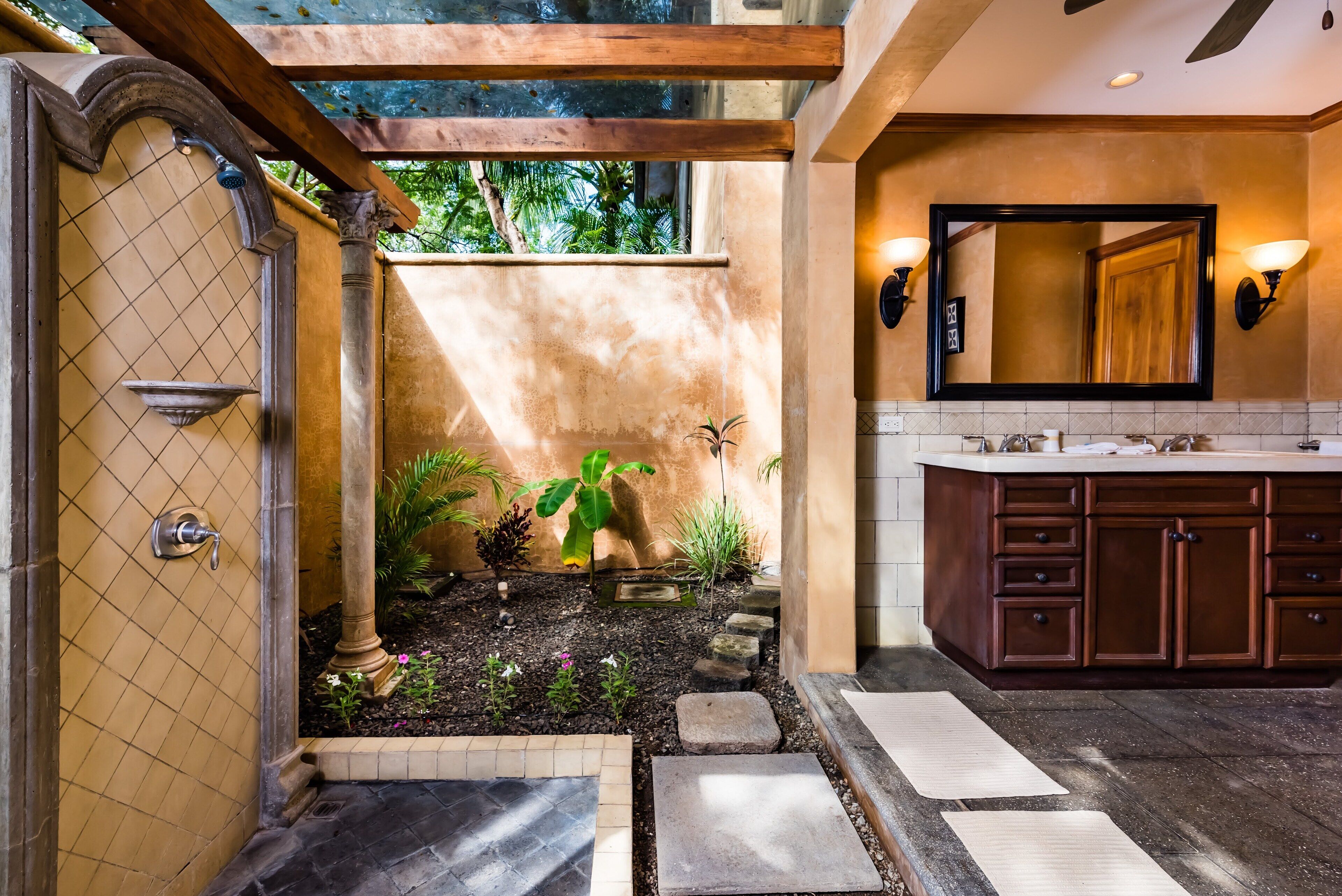 A bathroom with a stone pathway leading to a shower area, a large mirror, and a sink with wooden cabinets.