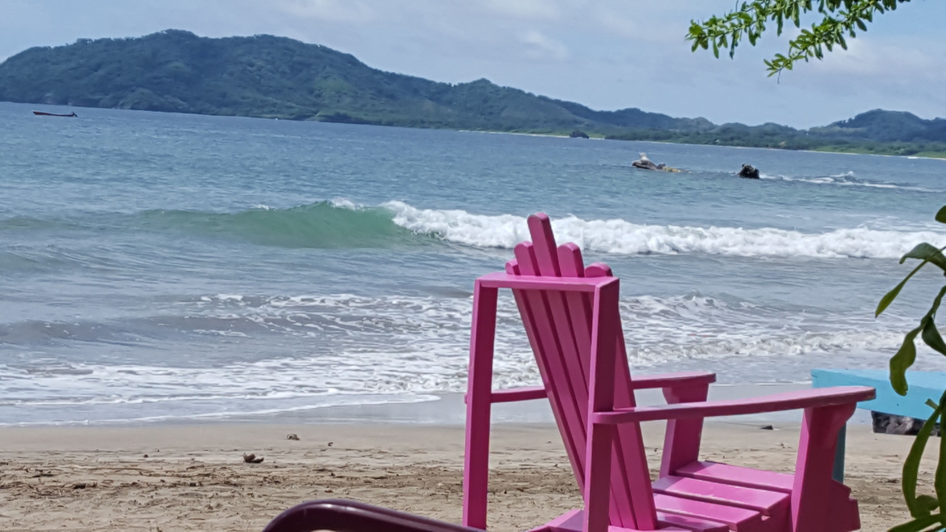 Une plage avec une chaise rose et une chaise bleue, toutes deux tournées vers l’océan.