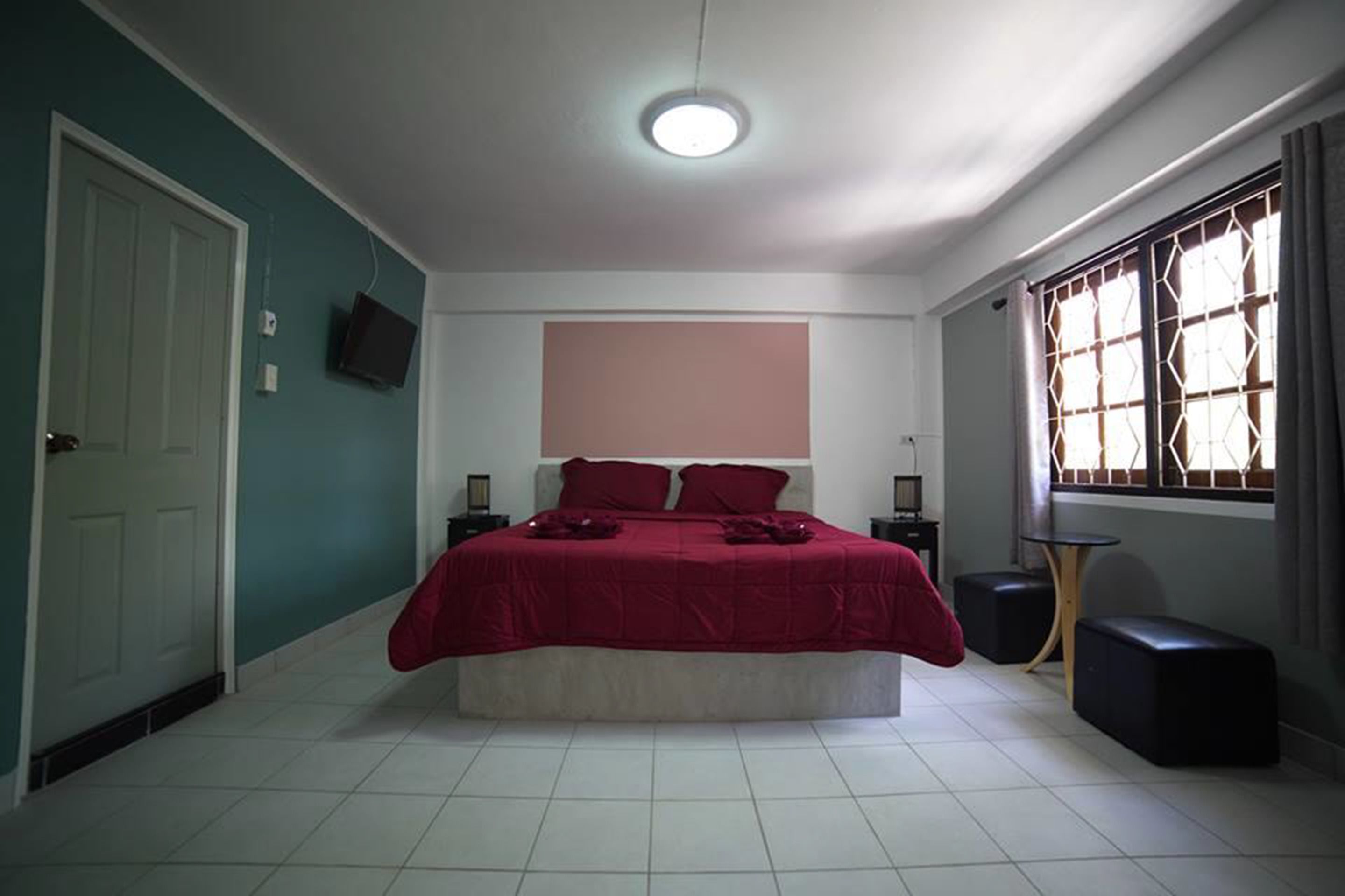 Ein Schlafzimmer mit einem Bett, einem Nachttisch, einem Fernseher und einem Fenster mit Vorhängen.