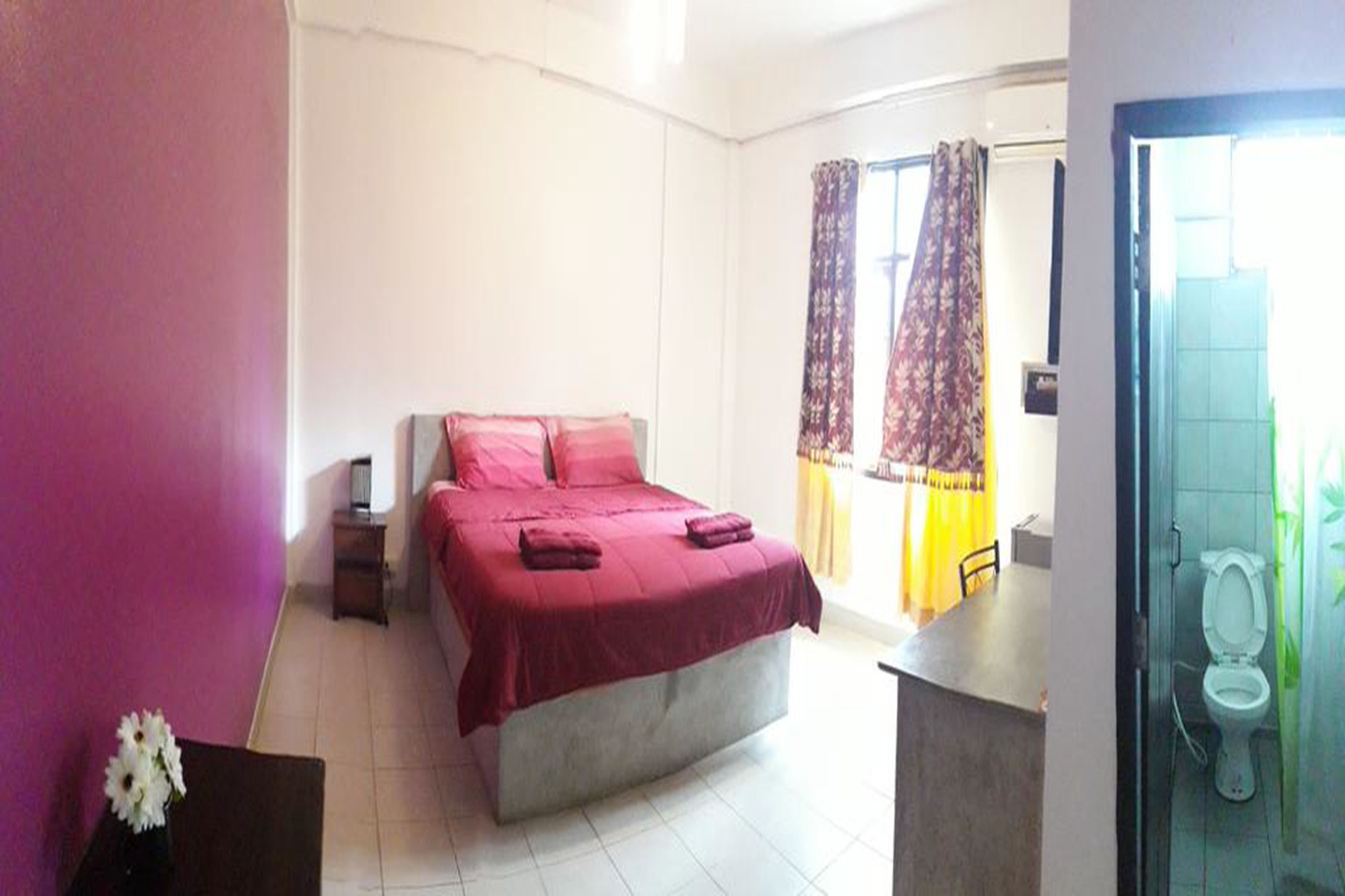 A bedroom with a bed, bedside table, and a bathroom with a toilet and shower.