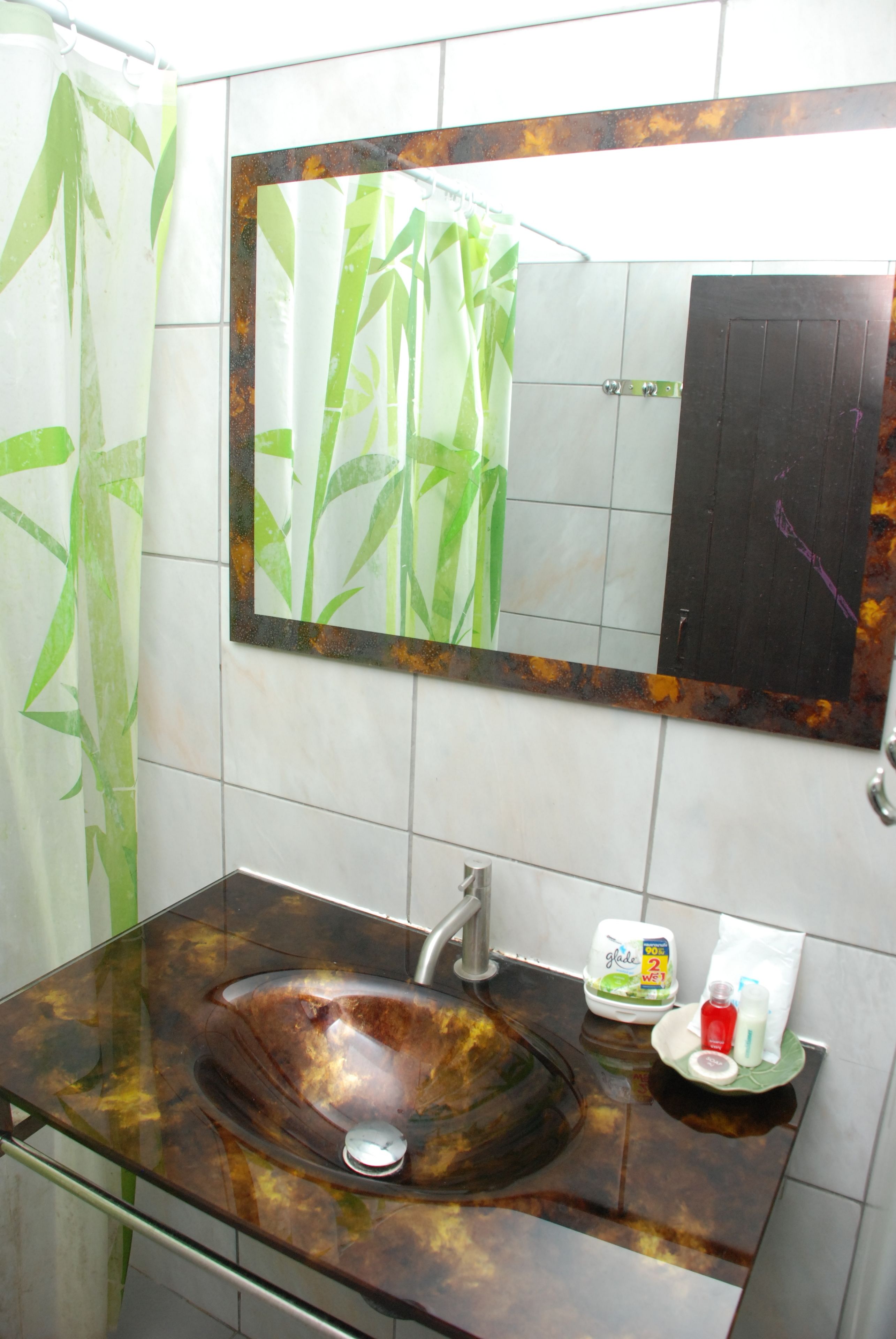 A bathroom with a glass sink, a mirror, and a shower curtain with a bamboo design.