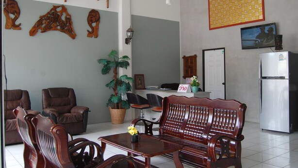 A living room with a wooden sofa, chairs, a small table, a fan, a potted plant, and a refrigerator. - Sea & Sand Guesthouse and Restaurant (Cha-am)