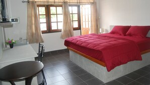 A bedroom with a bed, a desk, and a chair. There are curtains on the windows, and a small plant on the desk. - Sea & Sand Guesthouse and Restaurant (Cha-am)