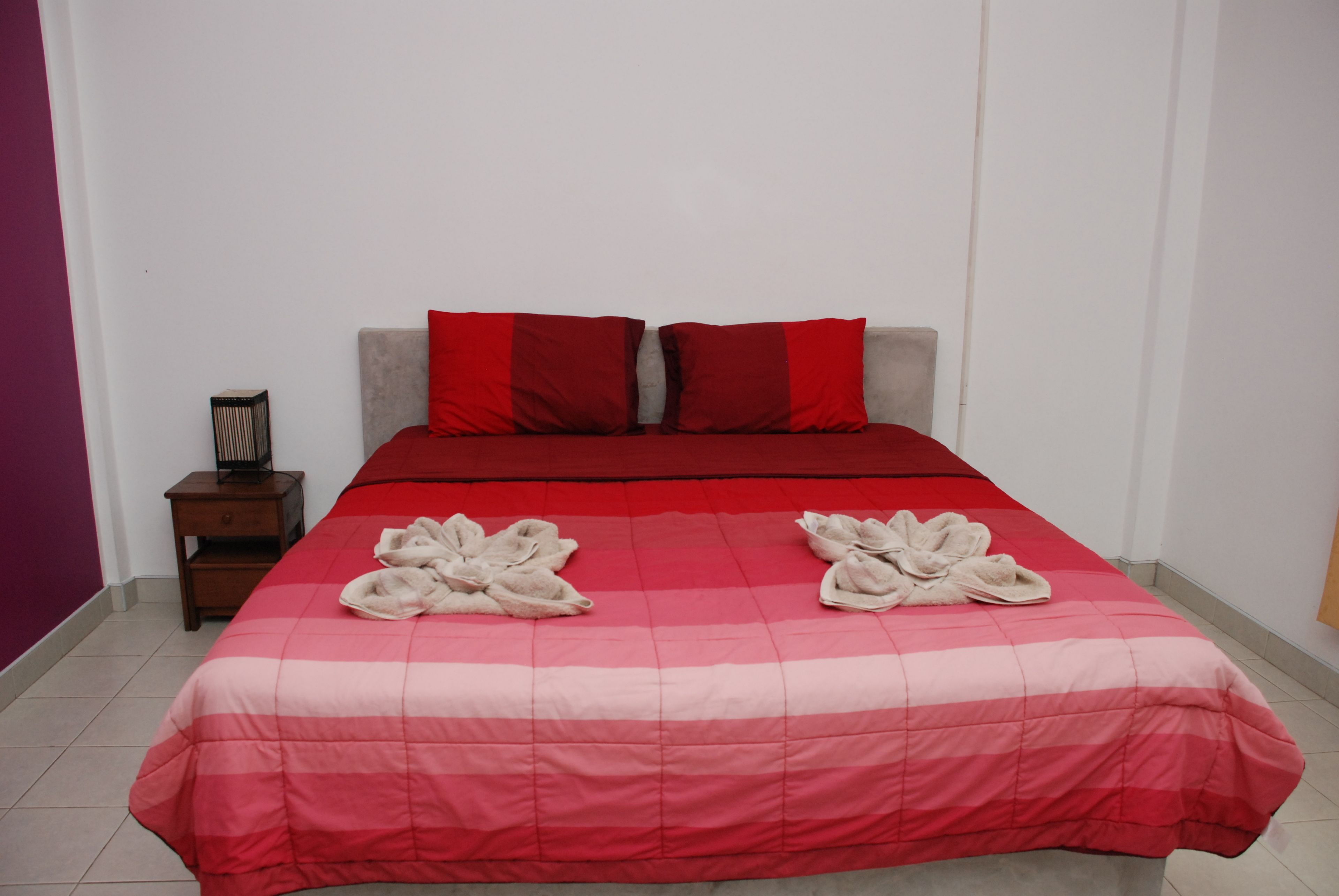 A neatly made bed with a red and pink bedspread, two red pillows, and two towels arranged on the bed.