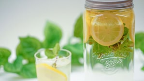 Un tarro de vidrio con una rodaja de limón y hojas de menta, y un vaso con una rodaja de limón y hojas de menta.