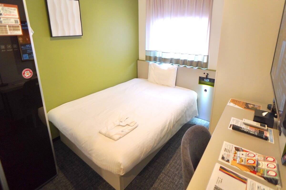A hotel room with a bed, a desk with a computer, and a window with curtains.