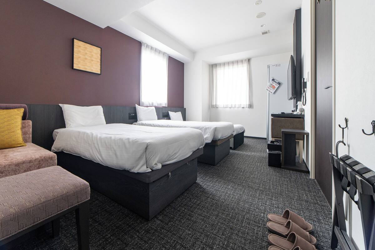 A hotel room with two beds, a desk, a chair, a TV, and a coat rack.