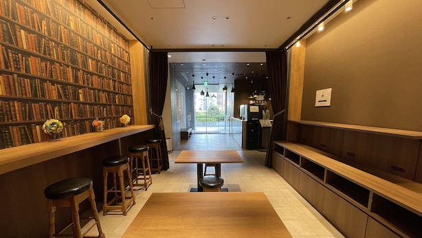 Un rincón de lectura con estanterías, una mesa de madera y taburetes de bar.