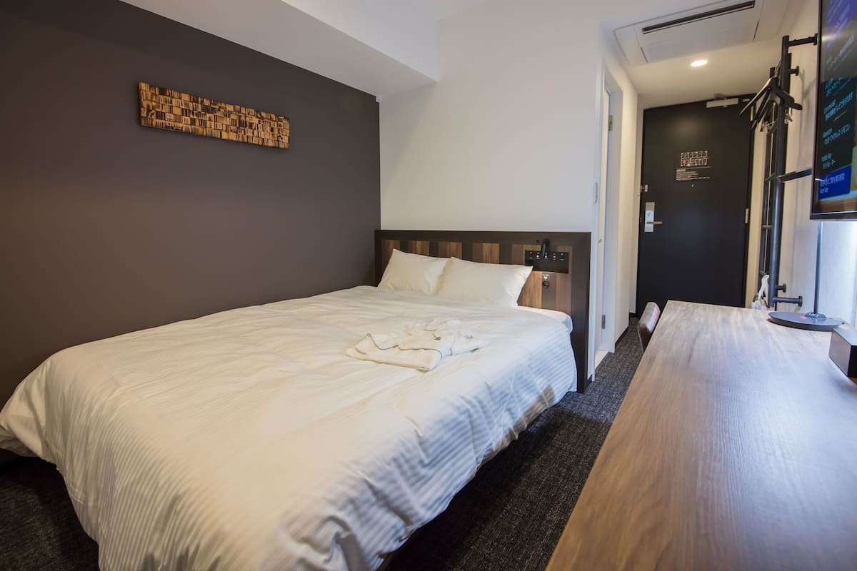 A hotel room with a large bed, a wooden headboard, a wall-mounted artwork, a flat-screen TV, and a wooden desk.