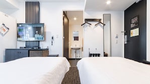 Habitación de hotel con dos camas, un escritorio con computadora, televisor, espejo y baño a la vista a través de una puerta abierta.