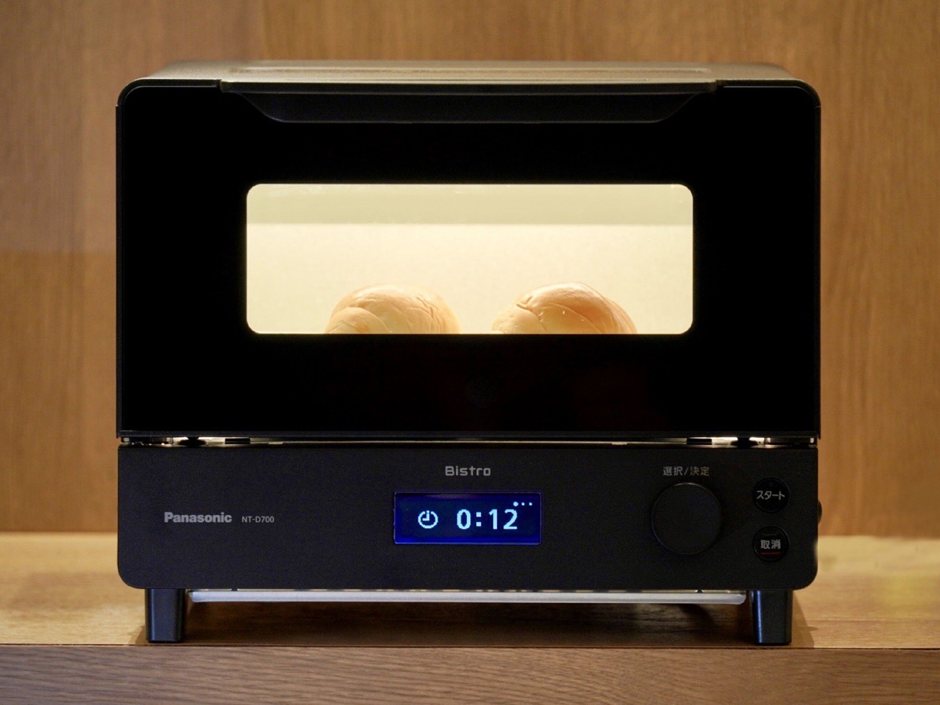 A Panasonic NT-D700 BISPRO microwave with a digital display showing 0:12, placed on a wooden surface.