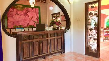 A reception desk with a large mirror, a laptop, and various certificates. There is a decorative archway and a door with a floral design.