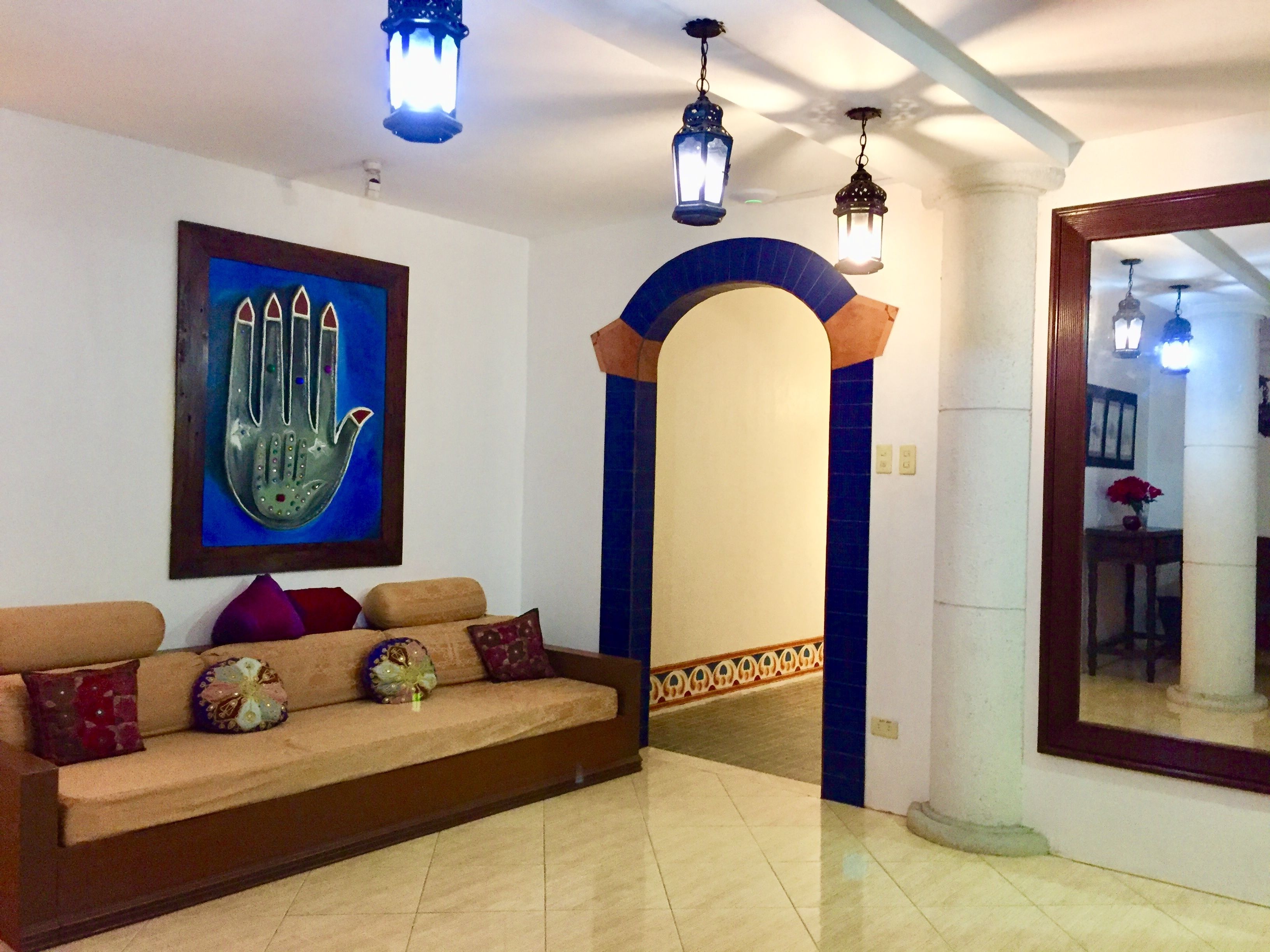 A living room with a sofa, decorative pillows, a wall-mounted artwork, and a hallway leading to another room.