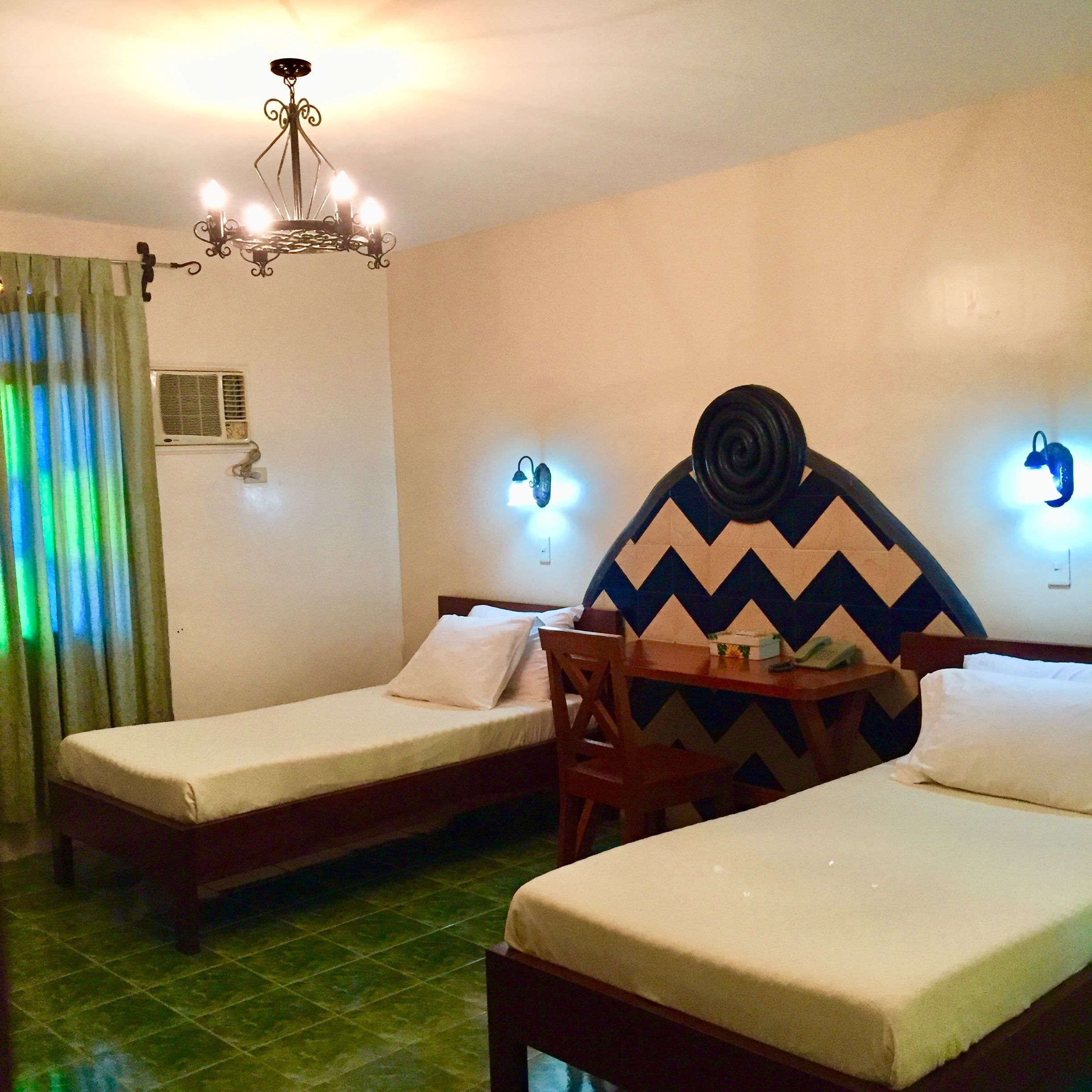 Una habitación de hotel con dos camas individuales, una mesa de madera, un candelabro y luces en la pared.
