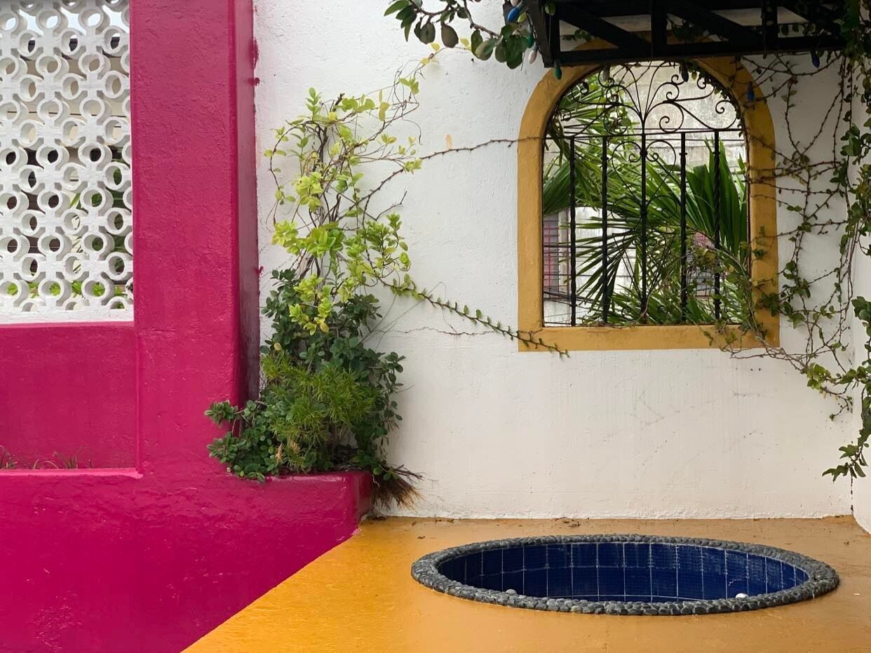Una piccola area piscina all'aperto con bordo piastrellato, circondata da un muro bianco con una sezione rosa e una sezione gialla.