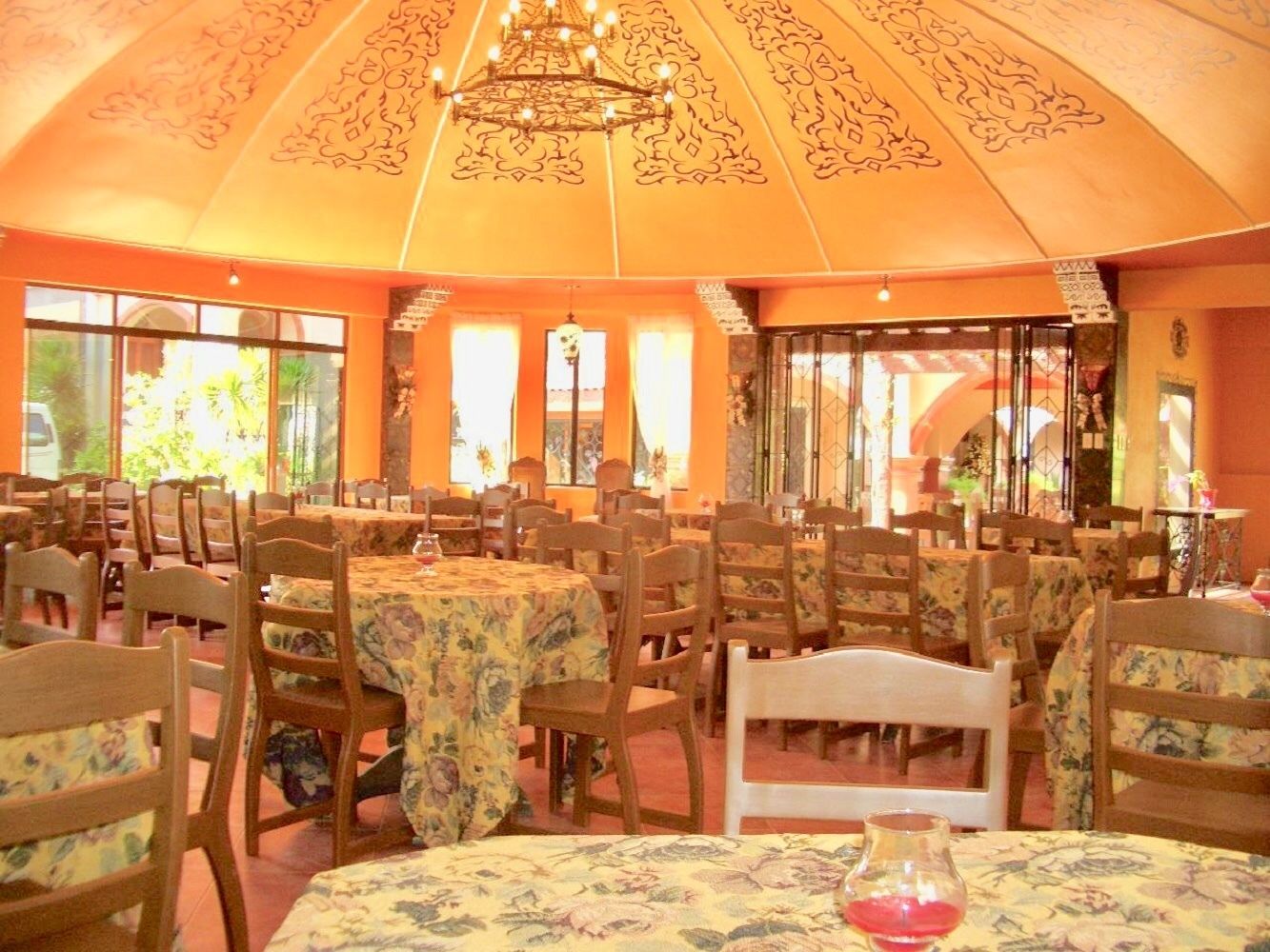 Un ristorante con diversi tavoli e sedie, ampie finestre e un soffitto decorato.