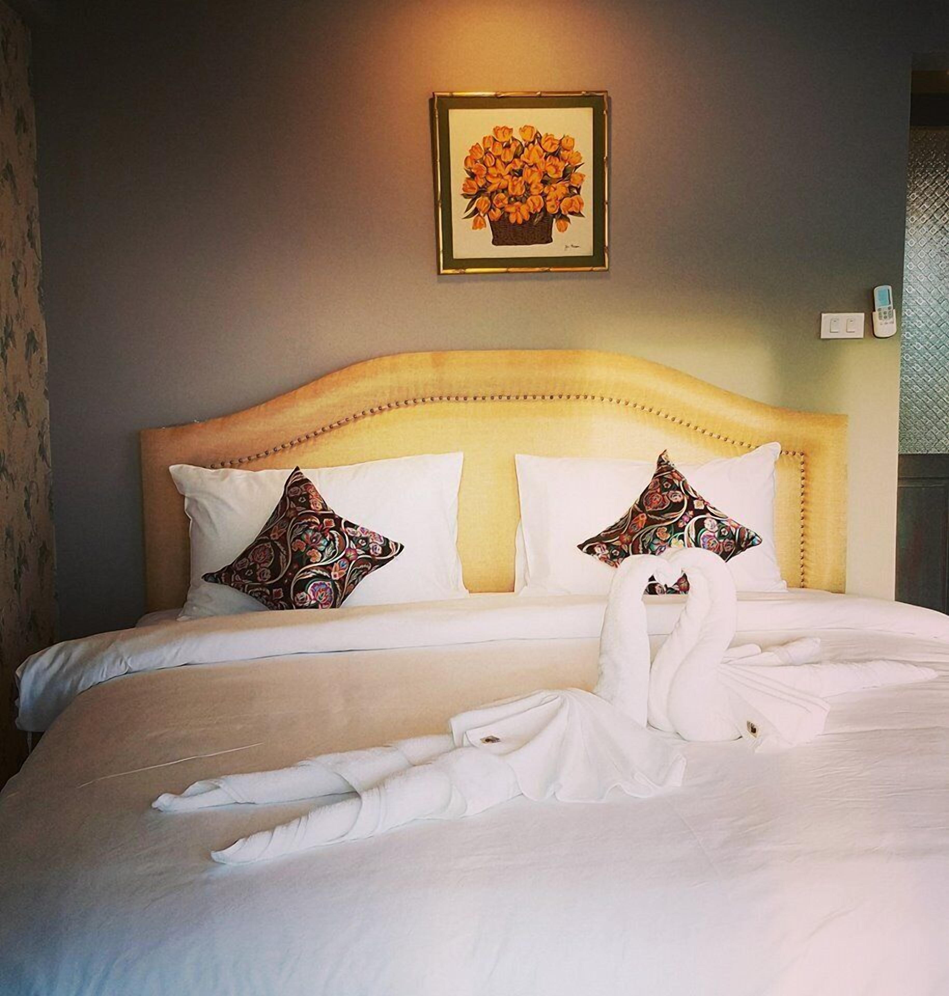 A neatly made bed with white linens and two decorative pillows, a framed floral artwork above the headboard, and a bedside telephone.