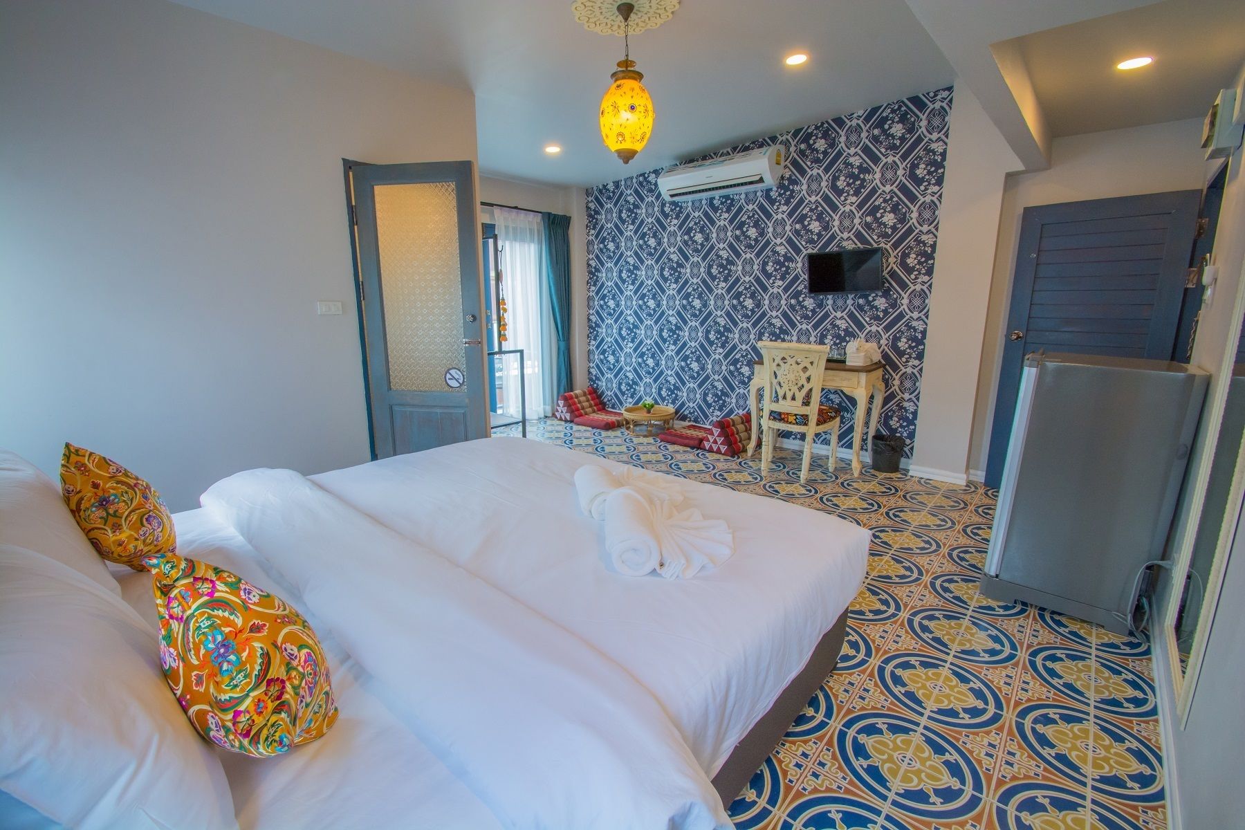 A hotel room with a large bed, a small table with chairs, an air conditioning unit, and patterned floor tiles.