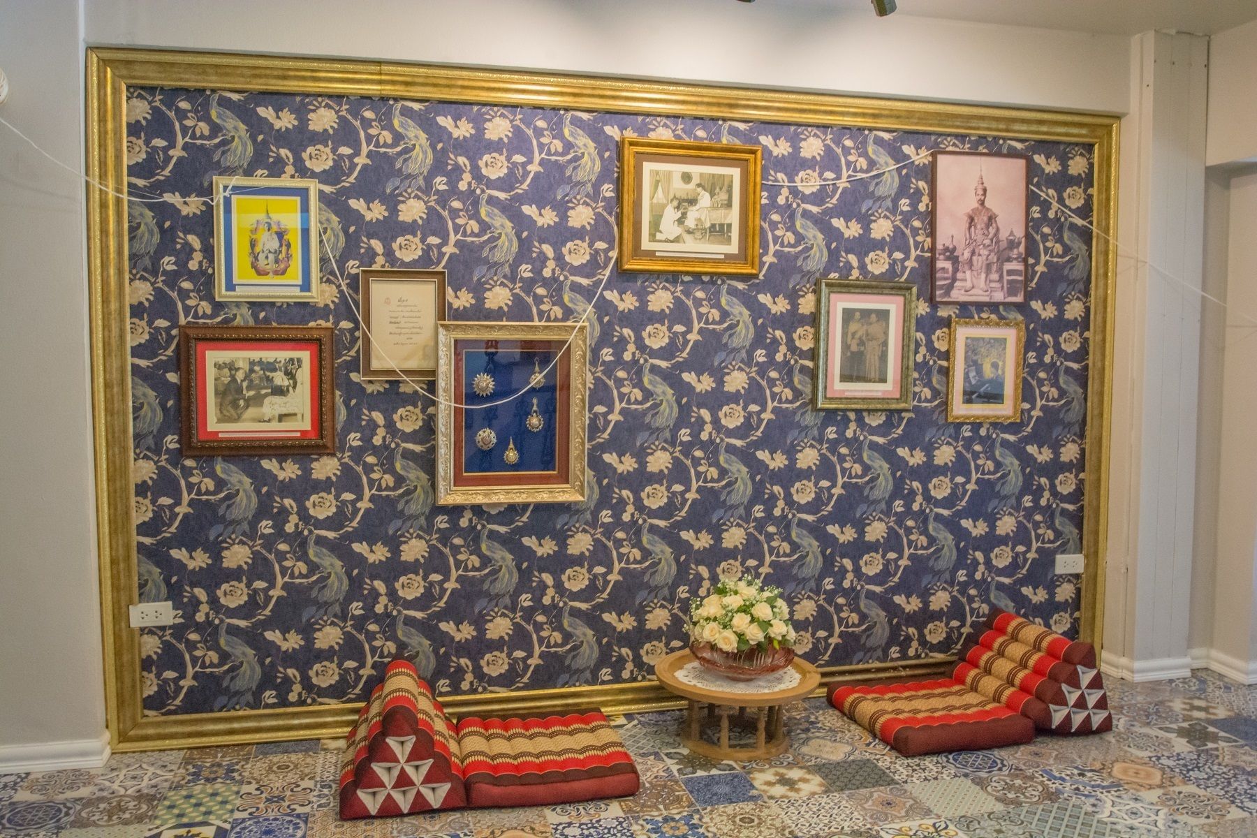 A room with a large floral-patterned wall, a small round table with a vase, and two red and beige cushions on the floor.