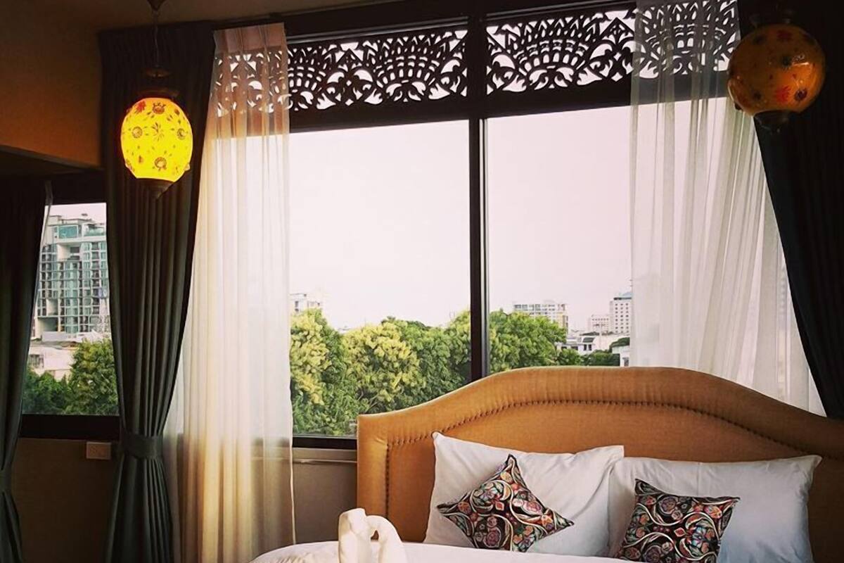 Ein Hotelzimmer mit Bett, Zierkissen, einem weißen Handtuch und Blick auf die Stadt durch große Fenster.