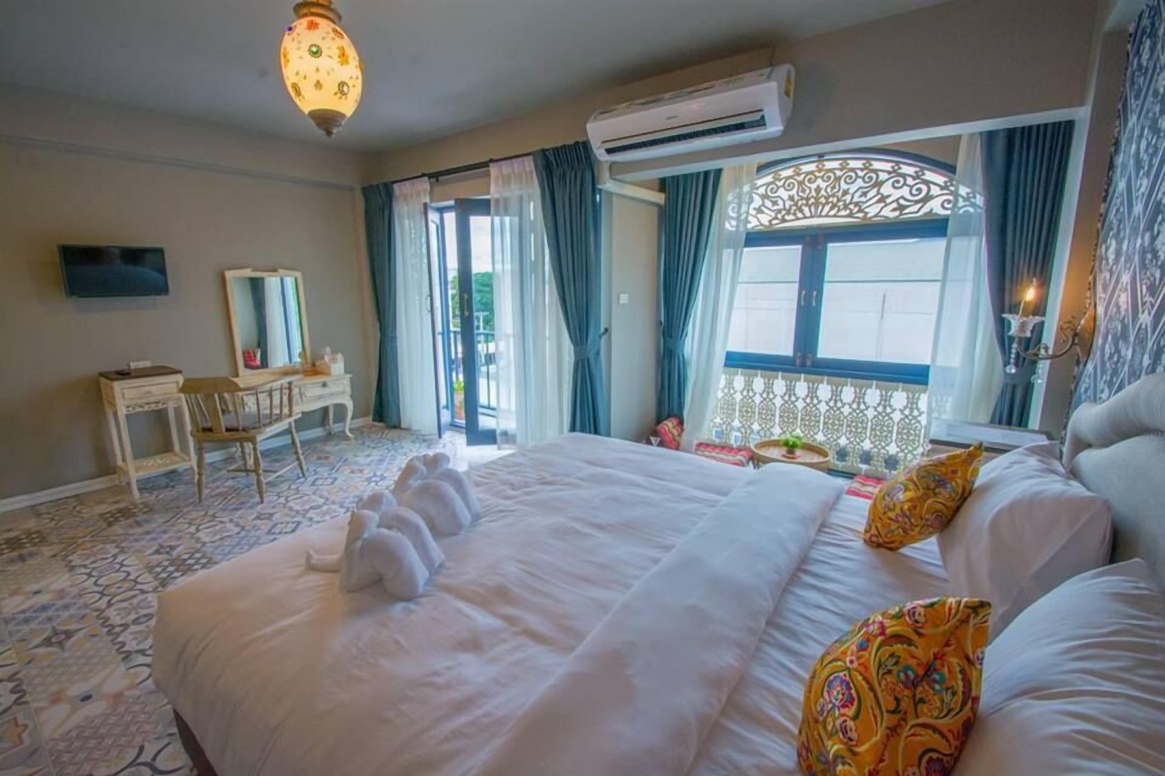 A hotel room with a large bed, a desk, a chair, a TV, and an air conditioning unit.