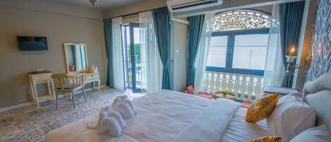 A hotel room with a large bed, a desk, a chair, a TV, and an air conditioning unit.