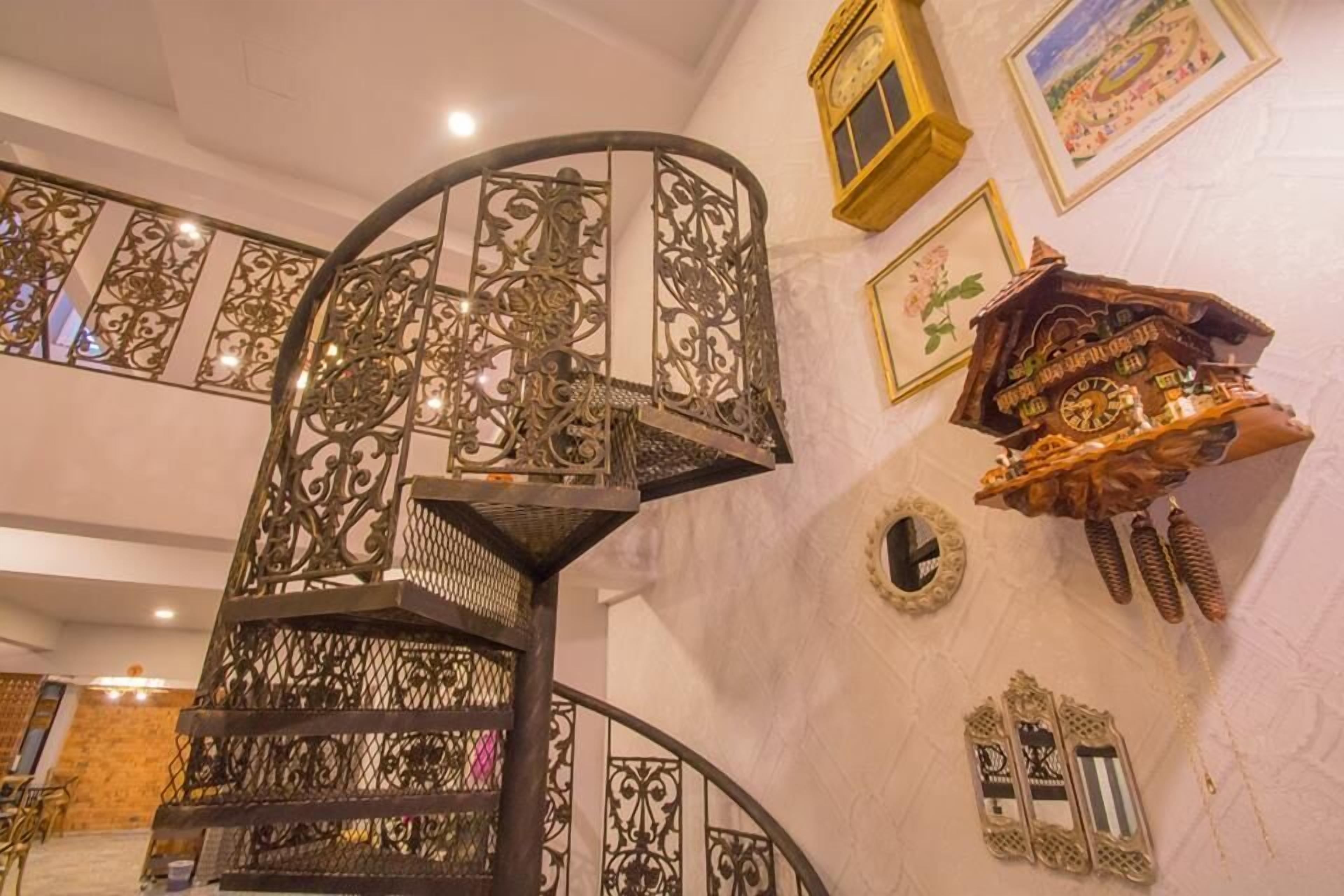 Een wenteltrap met sierlijk metalen hekwerk, een cuckoo klok en ingelijste foto's aan de muur.