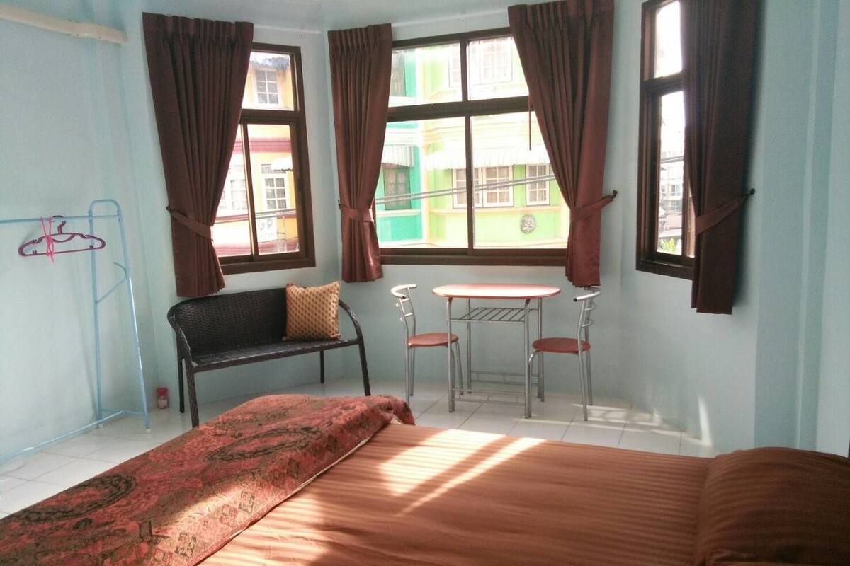 Une pièce comprenant un lit, une petite table avec deux chaises, un banc et une fenêtre avec des rideaux.
