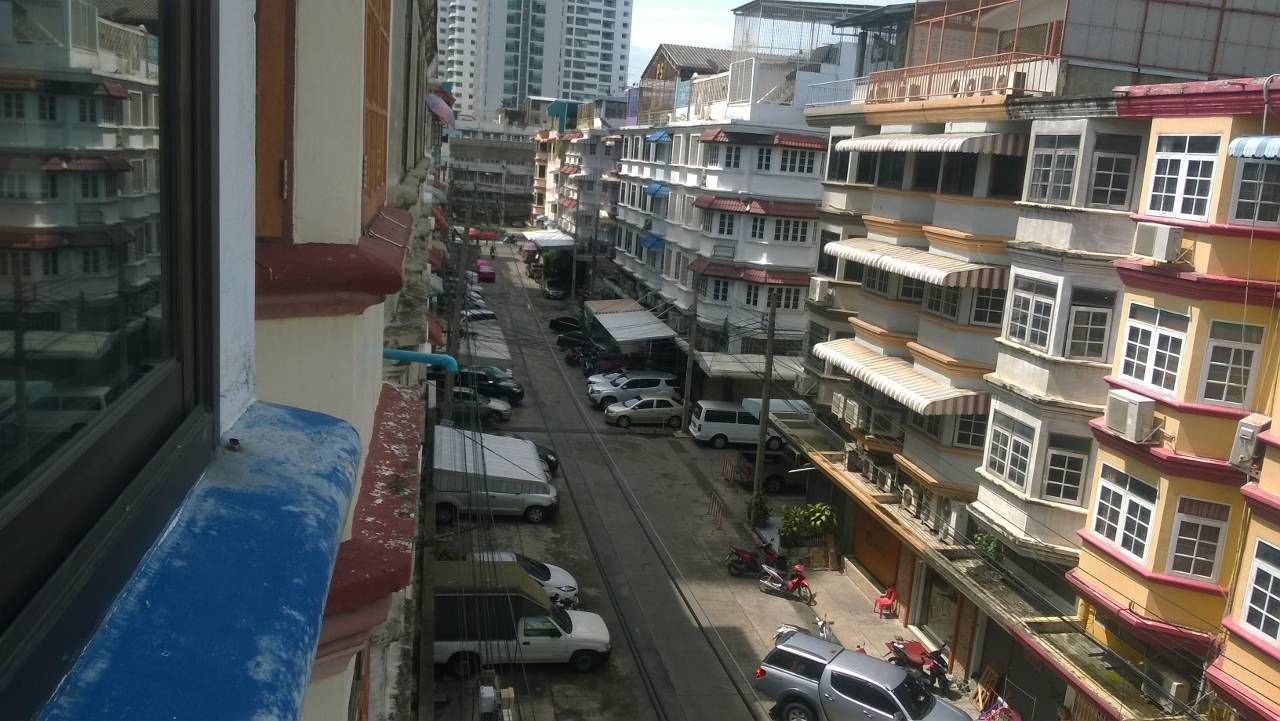 A narrow street lined with multi-story buildings, some with balconies and shops on the ground floor.