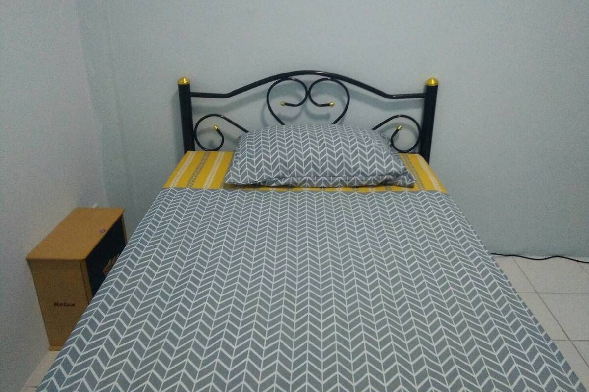 Un lit avec une couvre-lit à motifs et des oreillers, une table de chevet en bois et une boîte en carton étiquetée « Détente ».