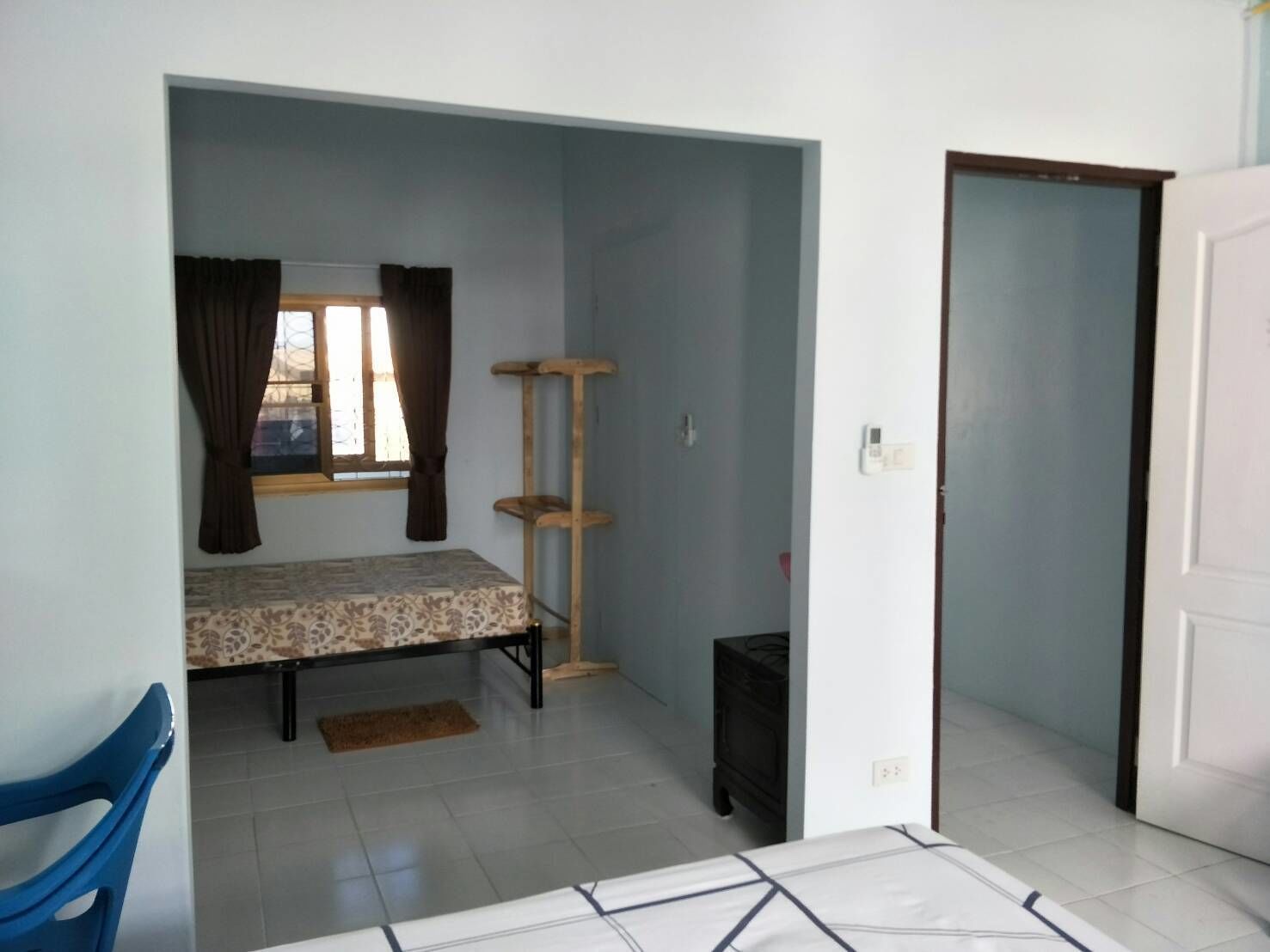 A small, sparsely furnished room with a bed, a cat tree, a chair, and a door leading to another room.