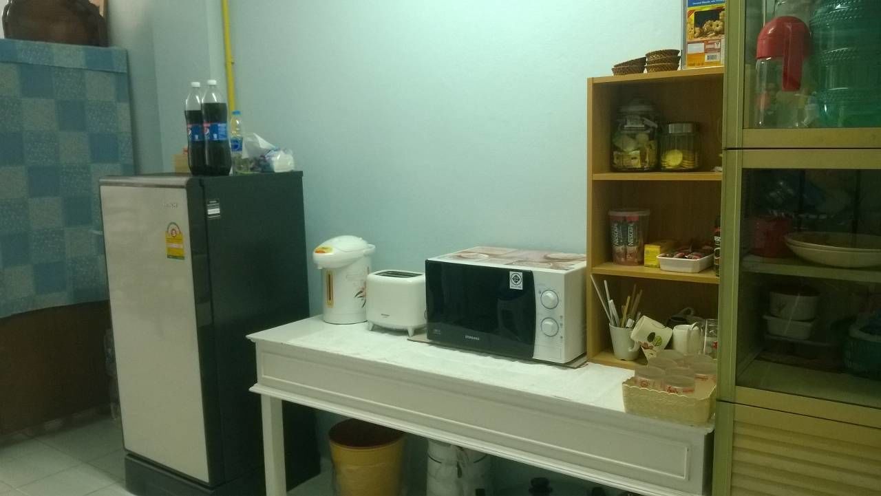 A compact kitchen with a refrigerator, microwave, toaster, and a small shelf with jars and containers.