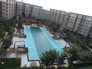 Una piscina rectangular grande rodeada de follaje y edificios modernos.