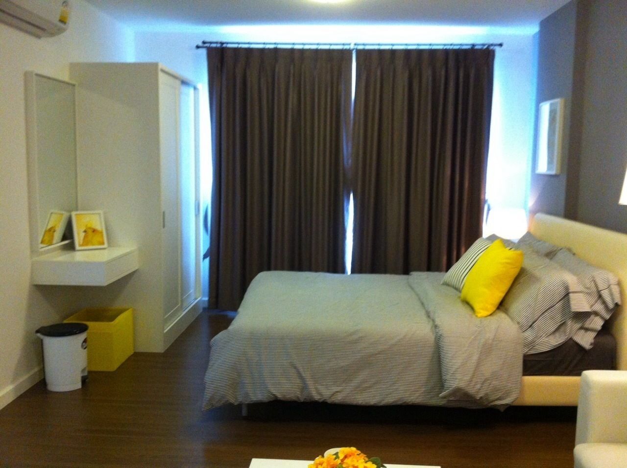 Un dormitorio con cama, cortinas, mesita de noche y un cubo de basura.
