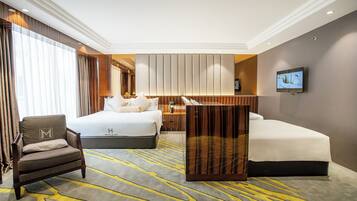 A hotel room with a large bed, a smaller bed, a sofa, a TV, and a desk.