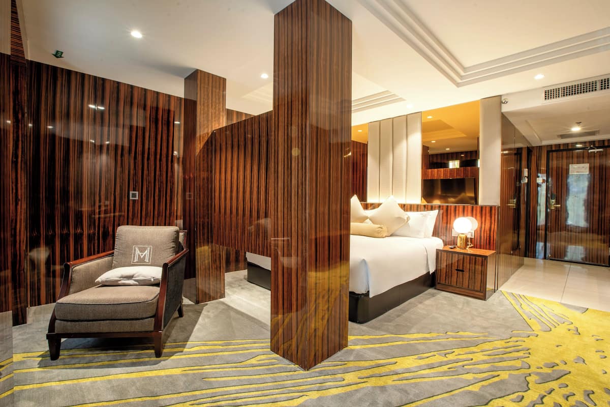 Une chambre d’hôtel moderne dotée d’un grand lit, d’un coin salon avec un fauteuil, d’une table de chevet et d’un grand miroir.