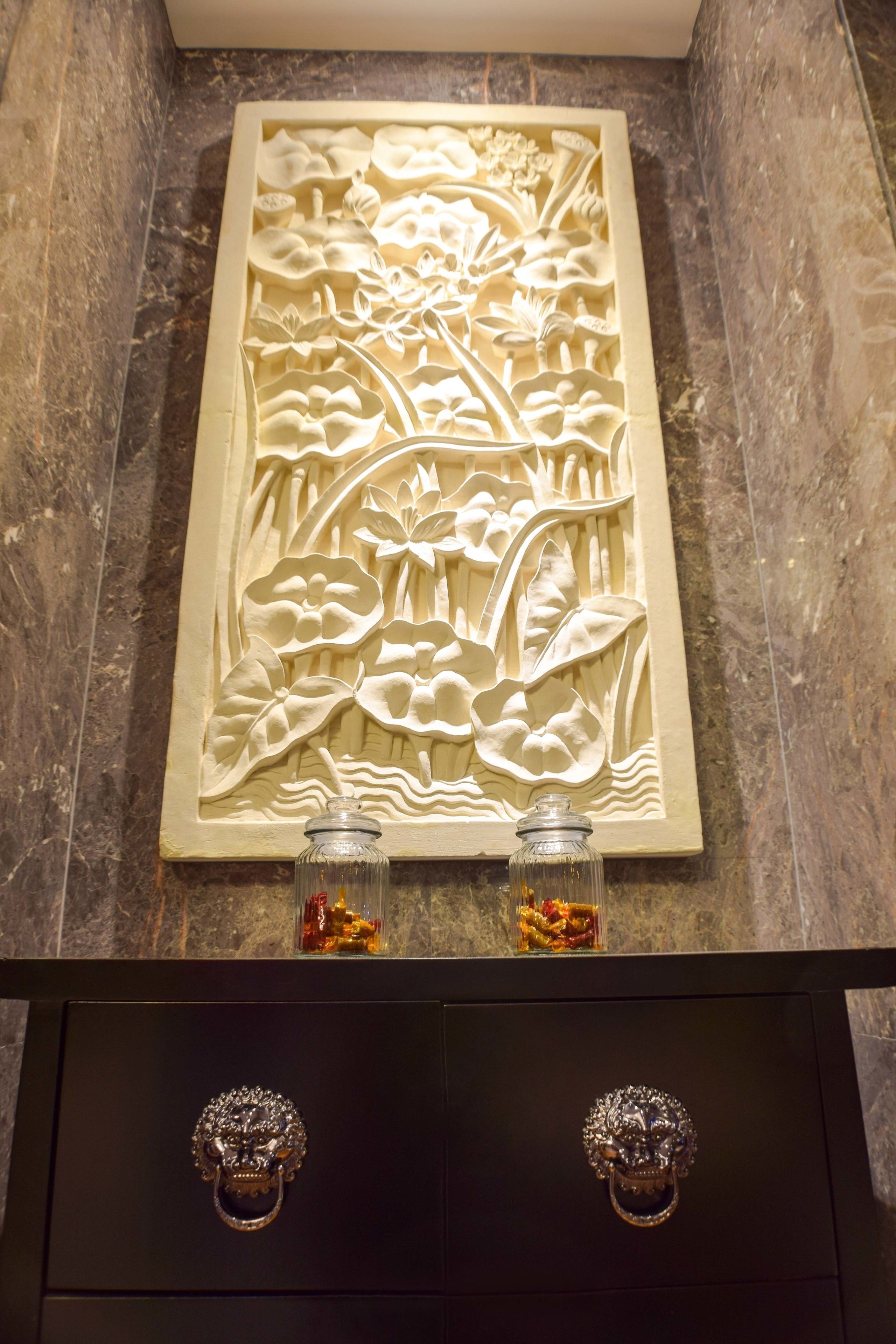 A wall with a floral carving and two small glass bottles.