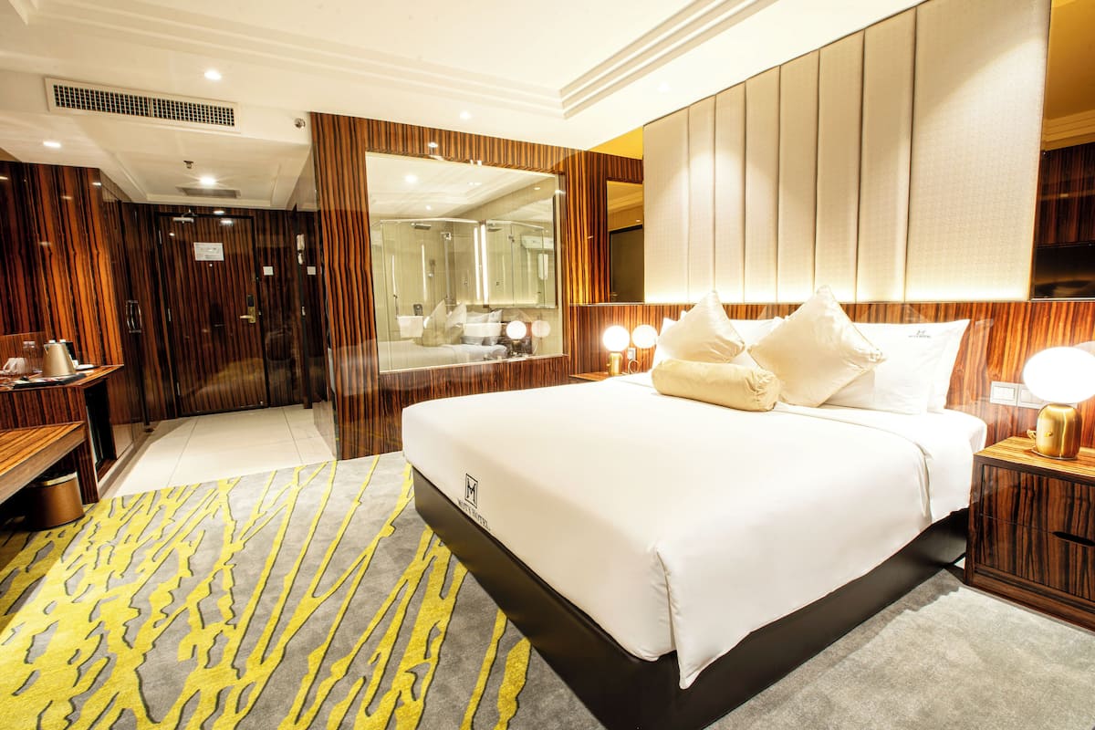 Une chambre d’hôtel avec un grand lit, une table de chevet en bois, un miroir et une salle de bain visible à travers une porte.