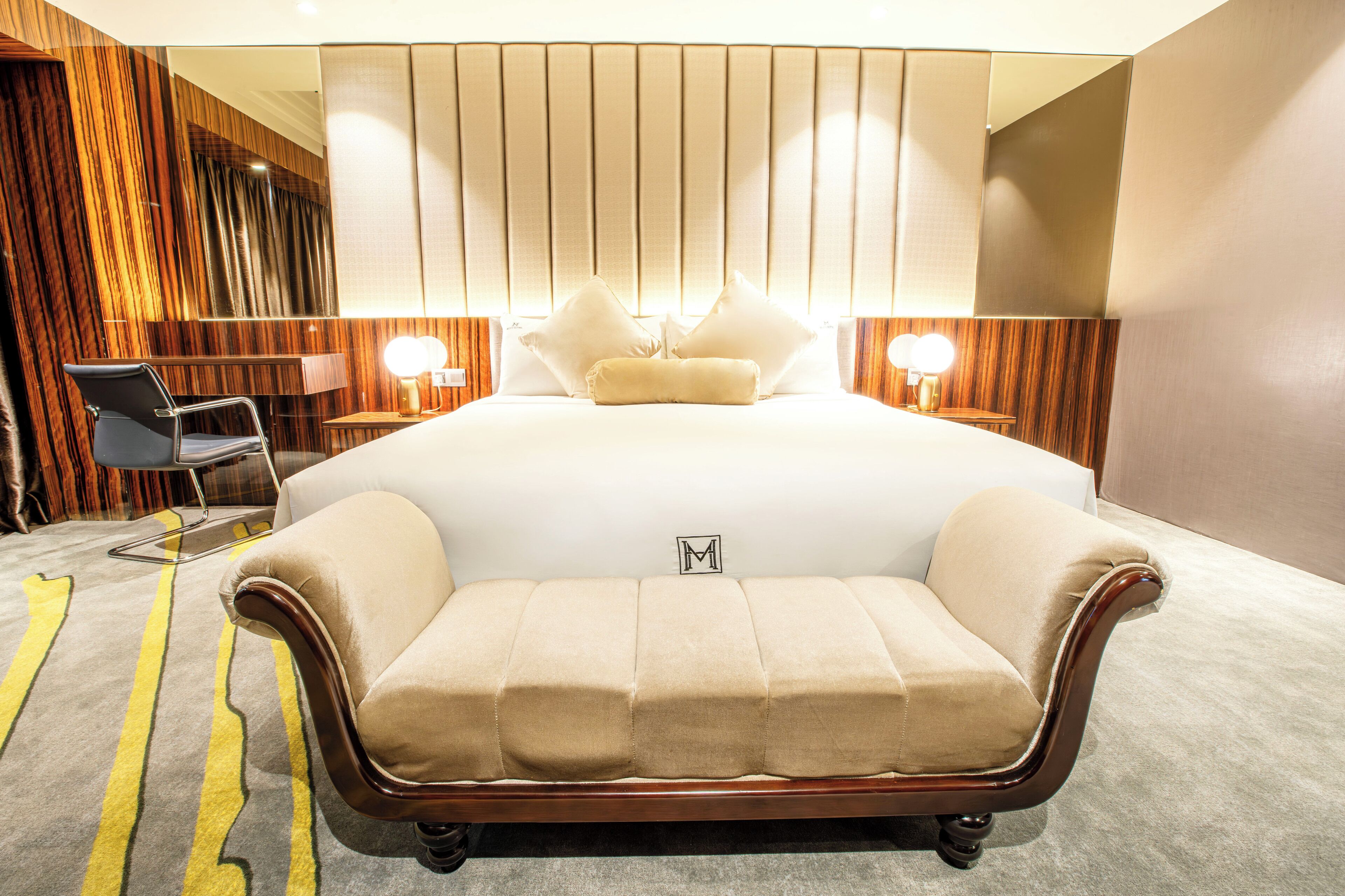 A hotel room with a large bed, a chaise lounge, a desk, and a mirror.