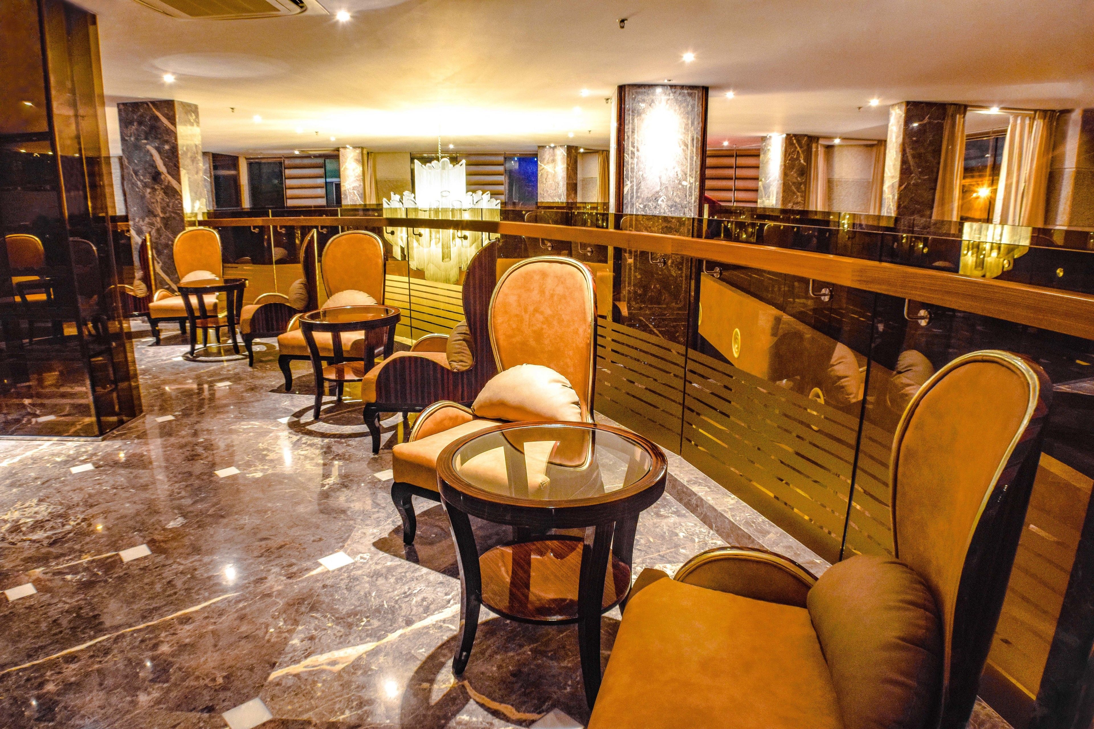 A lobby with marble flooring, multiple seating areas with cushioned chairs and round tables, and a reflective black reception desk.