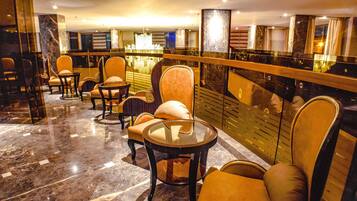 A lobby with marble flooring, multiple seating areas with cushioned chairs and round tables, and a reflective black reception desk.