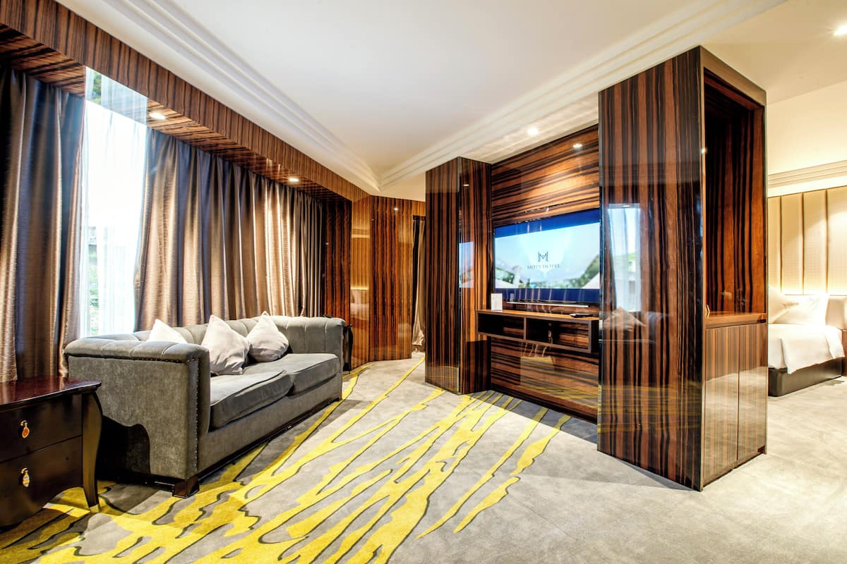 Une chambre d’hôtel moderne avec un canapé gris, un téléviseur à écran plat et un meuble de rangement en bois.