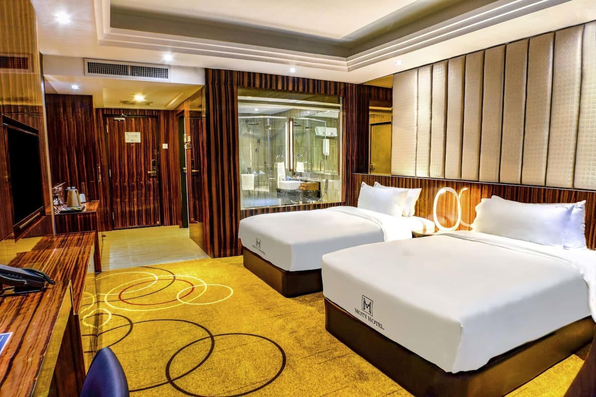 Une chambre d’hôtel avec deux lits, un bureau, un téléphone et une salle de bain visible à travers une paroi en verre.