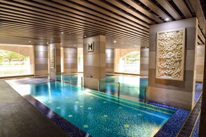 Una piscina interior con suelo de baldosas, techo de madera y un panel decorativo en la pared.
