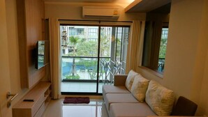 Un salón moderno con un sofá, un televisor y un balcón con vistas a zonas verdes.