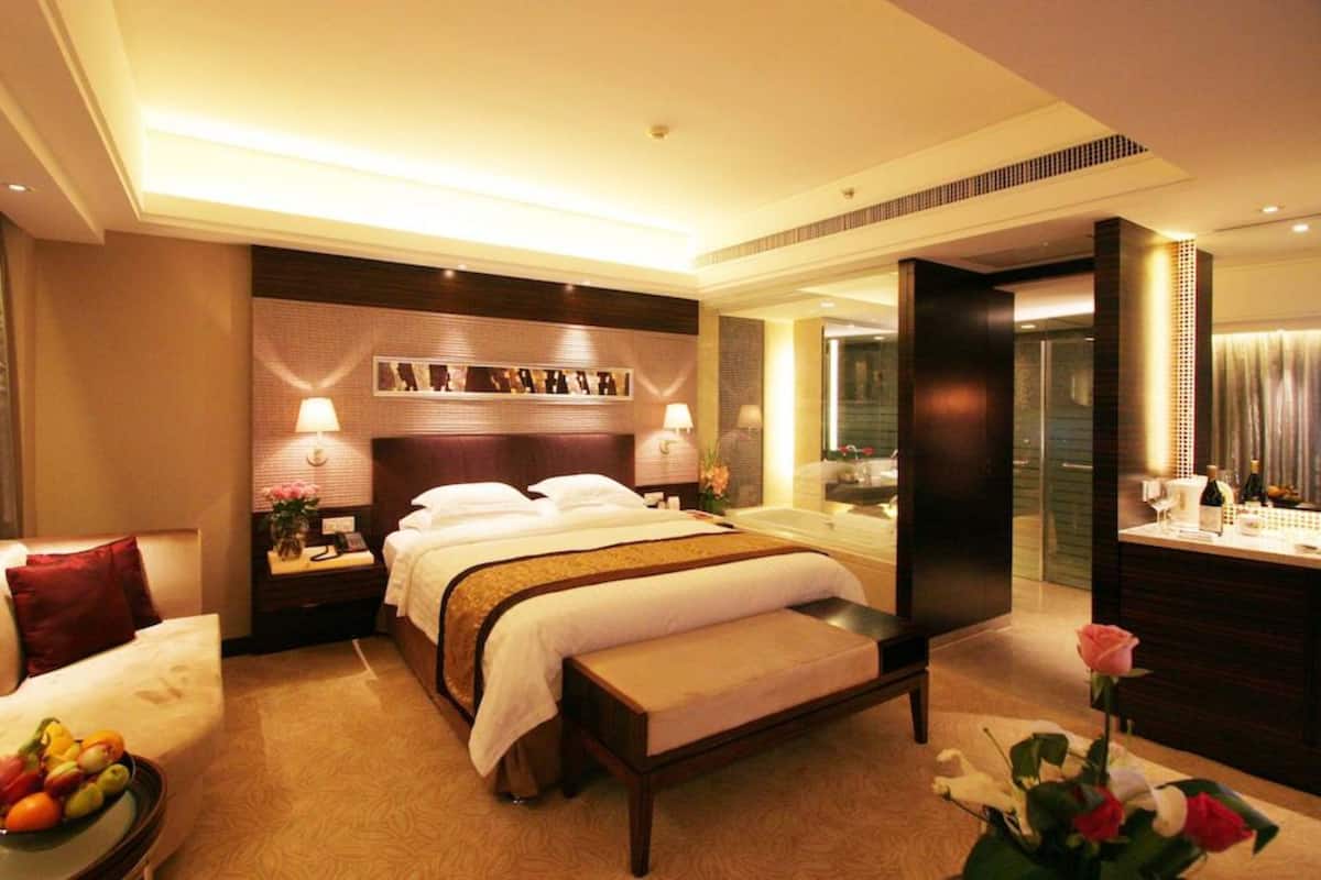 Hotelkamer met een groot bed, nachtkastjes, een bureau, een badkamer met spiegel en een zithoek met een bank en een schaal fruit.