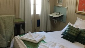 Ein Hotelzimmer mit einem Bett, einer grünen Tagesdecke, zwei weißen Handtüchern, einem grünen Kopfkissen, einem kleinen Tisch mit Stuhl, einem Fenster mit Vorhängen und einem wandmontierten Waschbecken.