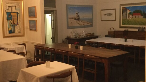 Ein Essbereich mit Tischen und Stühlen, ein Gemälde mit Strandmotiv und ein gerahmtes abstraktes Bild an der Wand.