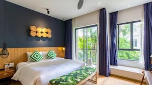 Quarto com uma cama grande, cabeceira de madeira e vista para o verde pela janela.