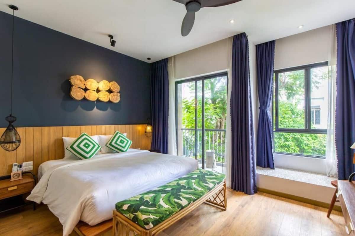 Une chambre avec un grand lit, une tête de lit en bois et une vue sur la verdure par la fenêtre.
